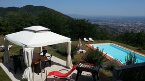 A pool area with a view of a cityscape, a covered seating area with chairs, and a foosball table.