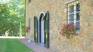 A stone building with a paved walkway, a door, and a window with a metal grille.