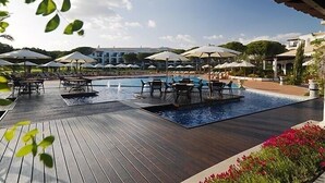 A pool area with lounge chairs and umbrellas, surrounded by a wooden deck and a pool. - Luxury villa V2, sleeps 6, Elevator to the beach, Cliff, Pine Cliffs Golf (Olhos de Agua)