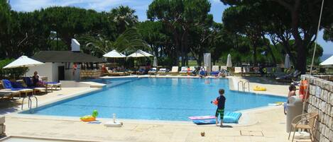 A swimming pool with lounge chairs and umbrellas, surrounded by trees.