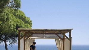 A wooden gazebo with a person lying on a massage table, another person attending to them, and a view of the sea. - Luxury villa V2, sleeps 6, Elevator to the beach, Cliff, Pine Cliffs Golf (Olhos de Agua)