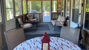 A covered outdoor seating area with wooden beams, large windows, and a table with a patterned tablecloth.