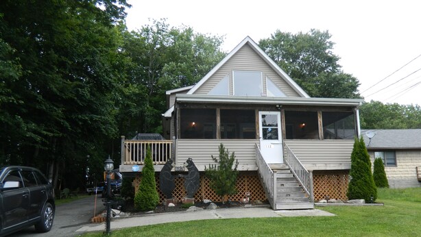 A two-story house with a front porch, a small deck, and a mailbox.