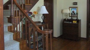 A wooden staircase with a glass enclosure at the top, a lamp, and a framed picture on a dark wooden side table.