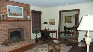 A living room with a brick fireplace, a sofa, a dining table with chairs, and a lamp.