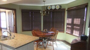 A kitchen with a granite countertop, a sink, a dining table with chairs, and a window with blinds.