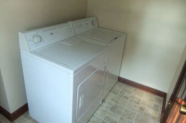 A compact, white front-loading washer and dryer unit in a small laundry room with tiled flooring and a wooden baseboard. - Country Farm Home, Travel the Bourbon Trail, & Historic Site (Bradfordsville)