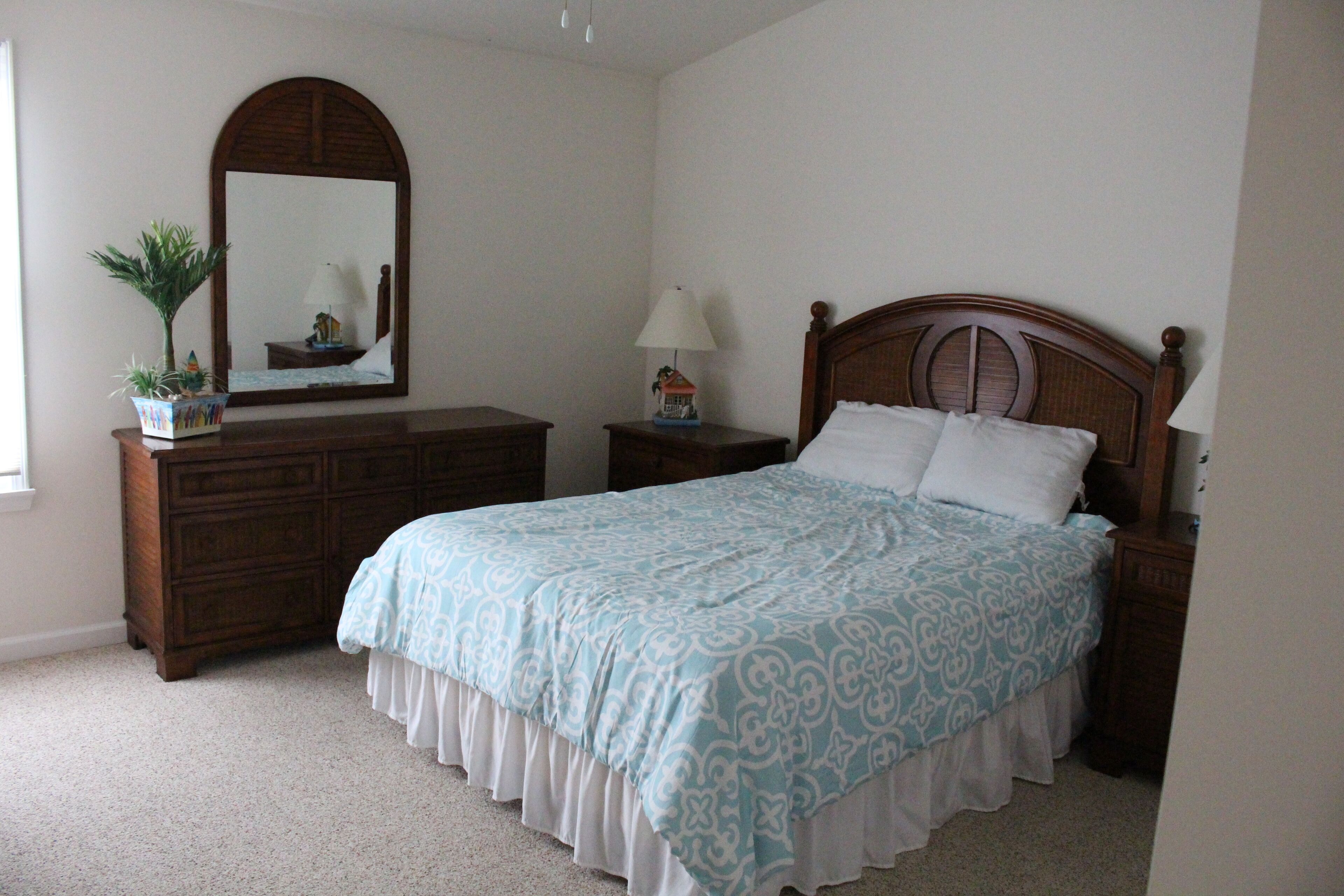 A bedroom with a large bed, a dresser, a nightstand, a lamp, a mirror, and a potted plant.