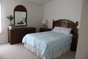Ein Schlafzimmer mit einem großen Bett, einem Schminktisch, einem Nachttisch, einer Lampe, einem Spiegel und einer Zimmerpflanze.