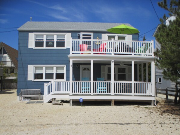 A two-story house with a balcony, a porch with chairs, and a green umbrella.