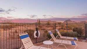 Un espacio al aire libre cercado con sillones de descanso y una pequeña mesa, con vista a un paisaje desértico y montañas al fondo.