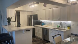 Cocina moderna con armarios blancos, electrodomésticos de acero inoxidable y una isla central con lavamanos y una pequeña planta.