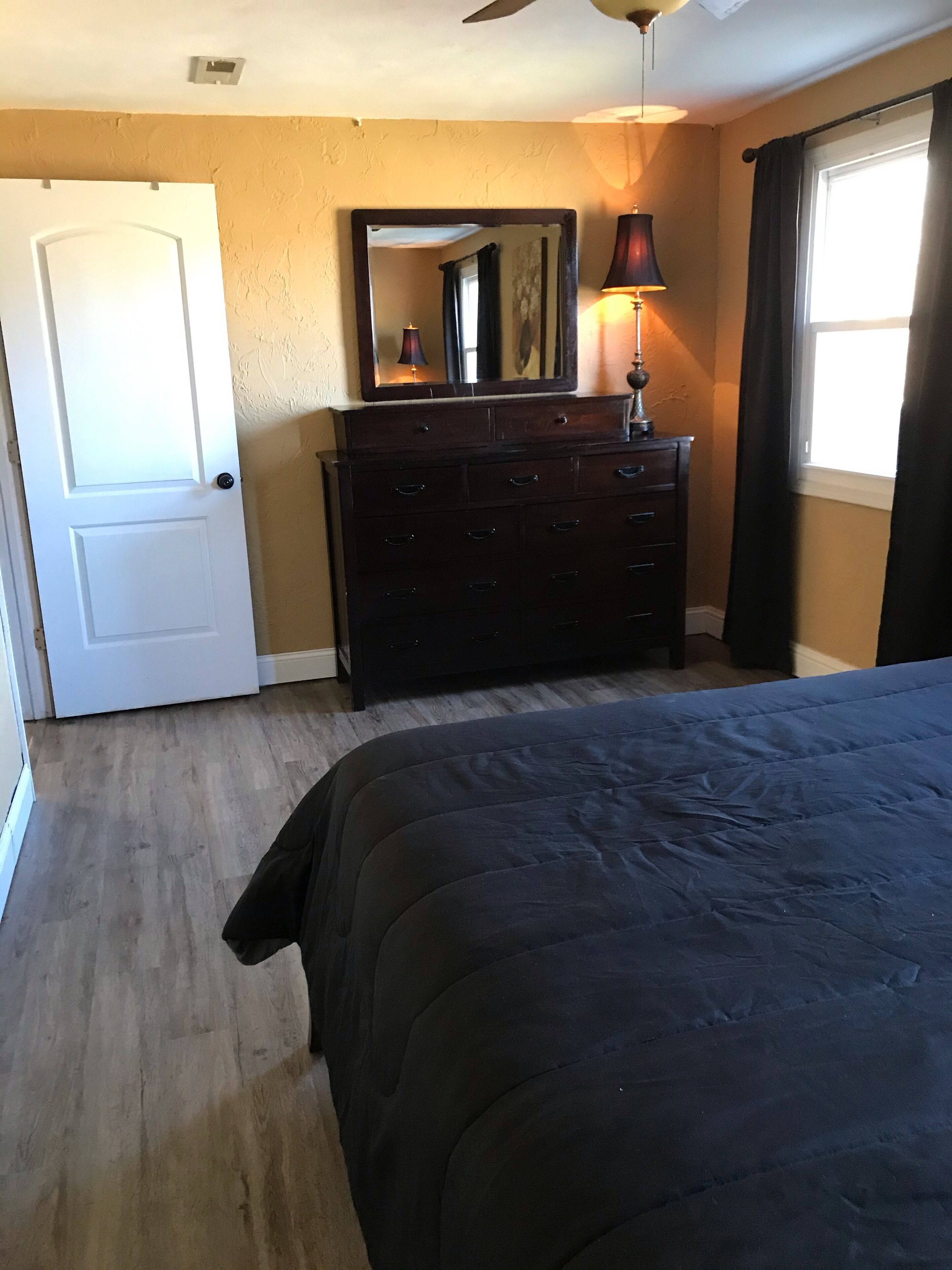 A bedroom with a bed, a dresser, a mirror, and a window with curtains.