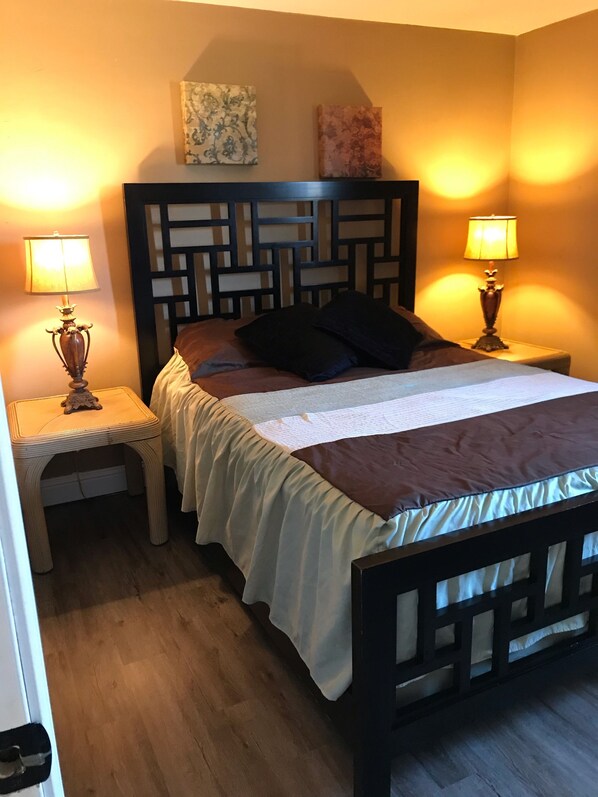 Un lit bien fait, avec une tête de lit en bois, deux tables de chevet avec des lampes et un petit tabouret.