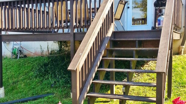 En trätrappa leder upp till en byggnad med en dörr och fönster. Vid trappans fot står två krukväxter med blommor.