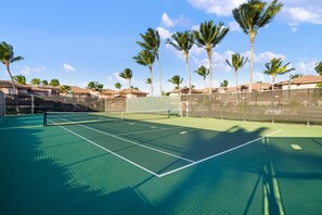 A tennis court with a net, surrounded by a fence and palm trees.