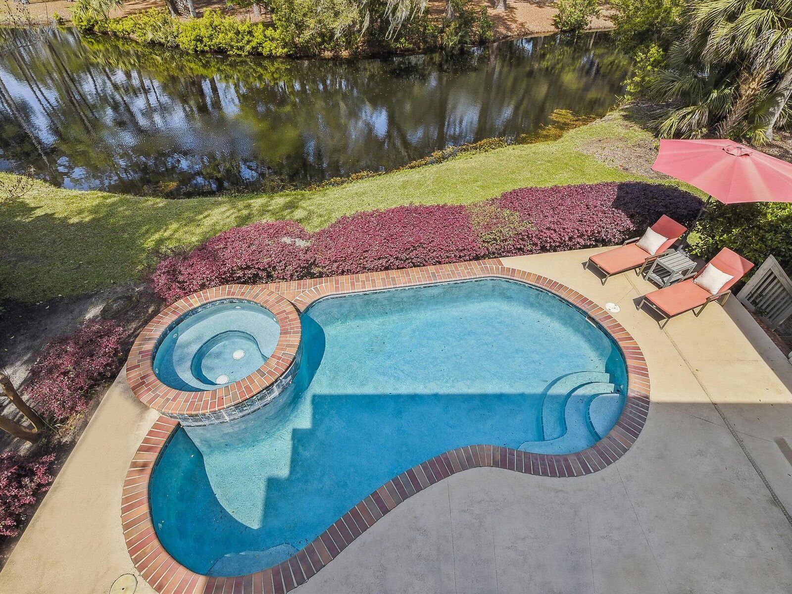 Een zwembad met een ronde hottub, omgeven door een metselwerkrand, en een klein terrasgedeelte met ligbedden en een rode parasol.