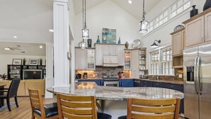 A spacious kitchen with a central island, wooden chairs, and a stainless steel refrigerator. - Stunning Lagoon & Harbour Town Golf Views! 2 Master Suites! (Hilton Head Island)