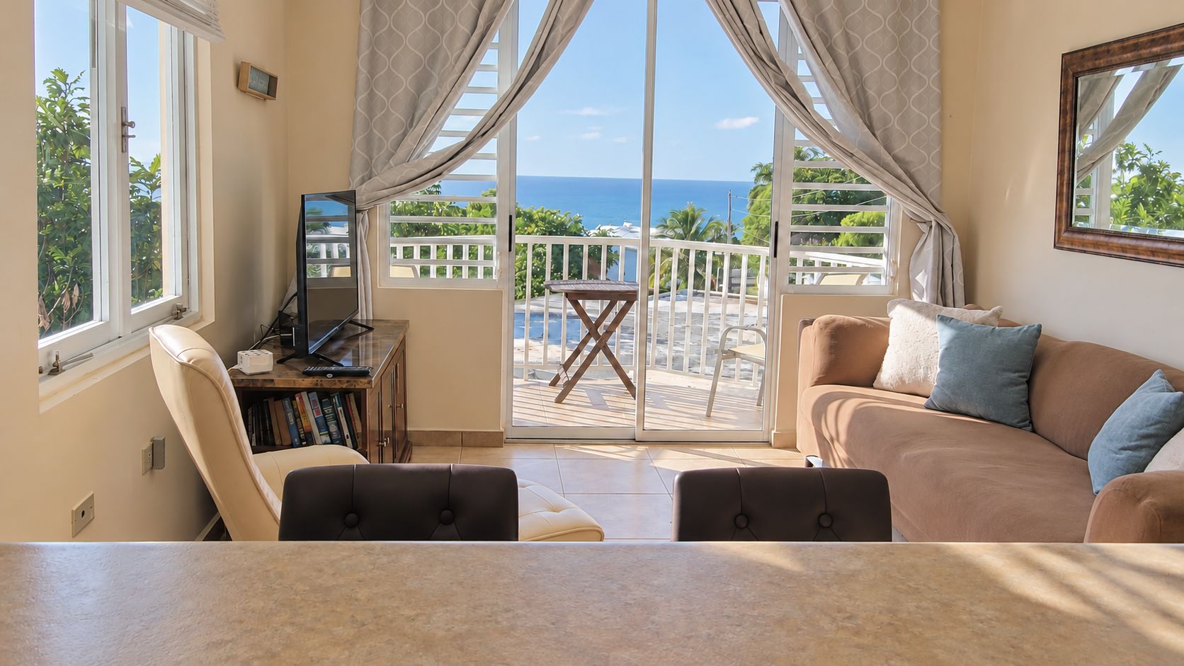 A living room with a view of the ocean, a sofa, a television, and a bookshelf.