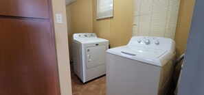 A laundry room with a washer and dryer, wooden door, beige walls, and a window with blinds.