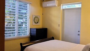 A bedroom with a bed, a dresser, a door, and an air conditioning unit. - WaveView - Rincon Apartment Rentals:  Puntas 1  BR Condo w/ Ocean View (Puntas Rincon)