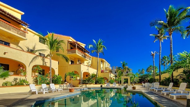 Un resort con piscina cristalina, palmeras y un edificio amarillo con balcones.
