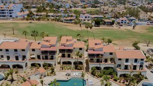 Un hotel de varios pisos con piscina, rodeado de palmeras y un campo de golf.