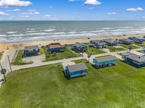 An aerial view of a coastal residential area with houses, a beach, and a clear sky.