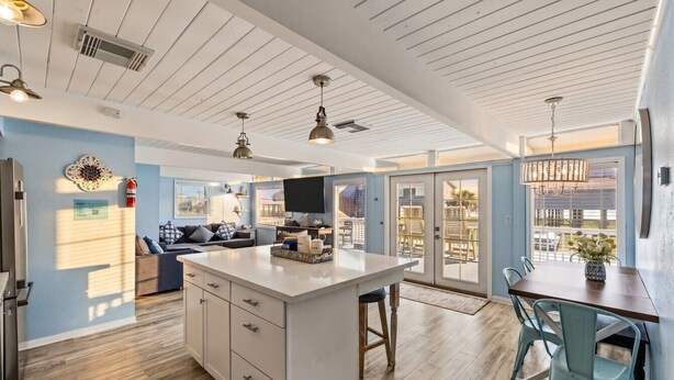 A spacious kitchen with a central island, a dining area with chairs, and a large sliding glass door leading to an outdoor patio. - Beach Cottage with Big Yard & Ocean Views (Galveston)