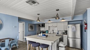 A modern kitchen with a central island, bar stools, a microwave, stove, and a refrigerator. - Beach Cottage with Big Yard & Ocean Views (Galveston)