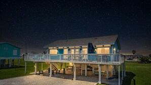 A house with a balcony, a covered porch, and a gravel driveway. - Beach Cottage with Big Yard & Ocean Views (Galveston)