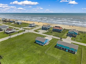 An aerial view of a coastal residential area with houses, a beach, and a clear sky.