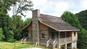 Une cabane rustique avec une cheminée en pierre, une véranda en bois et une allée gravillonnée.
