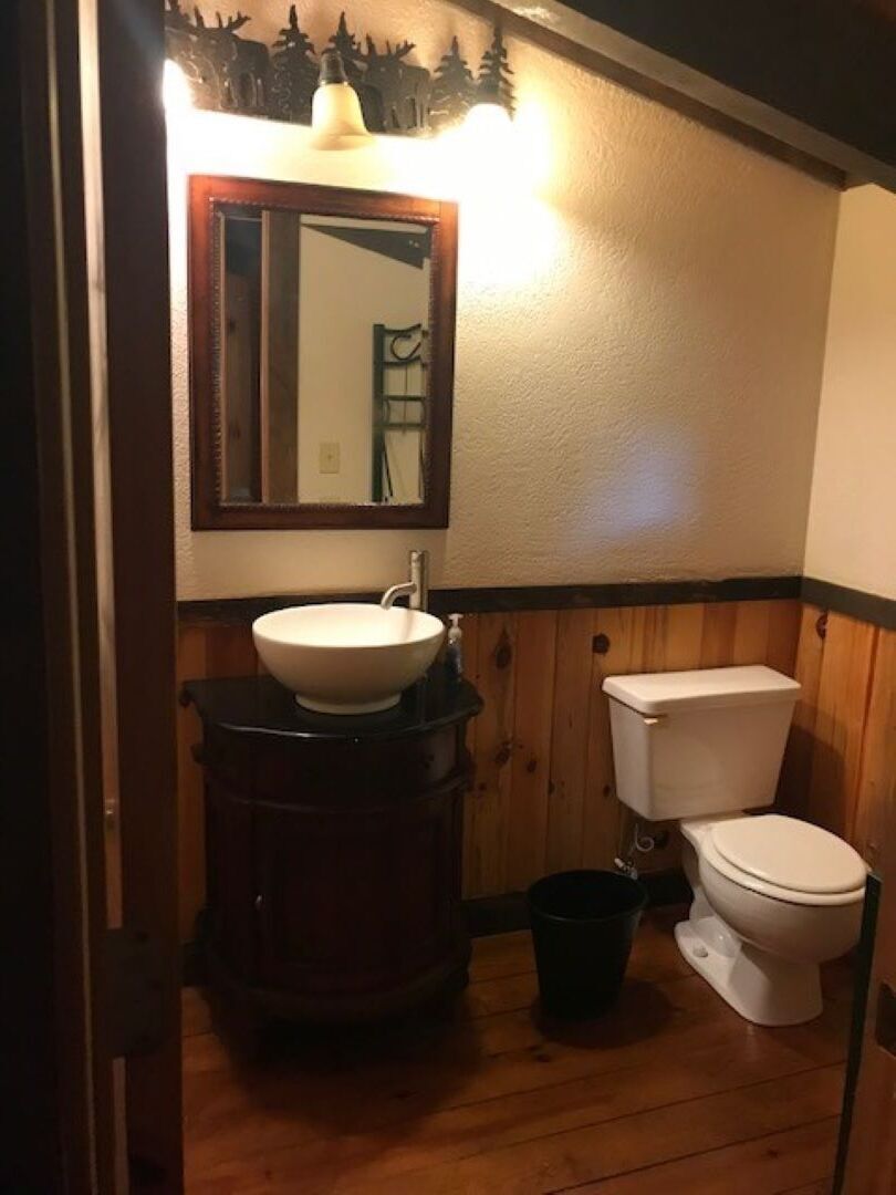 A bathroom with a wooden vanity, a white sink, a mirror, and a toilet.