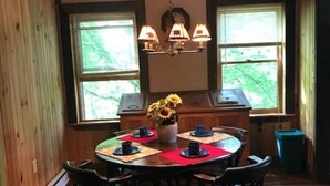 Un coin repas comprenant une table en bois, quatre chaises, un vase avec des fleurs et deux fenêtres équipées de stores.