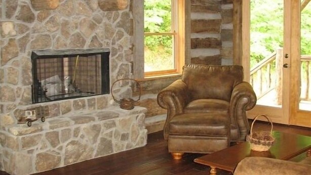 L’intérieur chaleureux d’un chalet avec une cheminée en pierre, des murs en bois et un coin salon confortable.