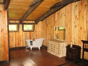 A wooden interior with a freestanding bathtub, a vanity with a mirror, and two windows. - Authentic Log Cabin in the Blue Ridge Mountains Family and Pet friendly (Newland)