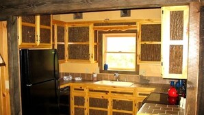Une cuisine compacte avec des meubles en bois, un réfrigérateur noir, un évier et une fenêtre qui laisse entrer la lumière naturelle.