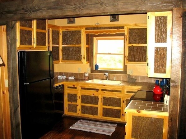 A compact kitchen with wooden cabinets, a black refrigerator, a sink, and a window providing natural light. - Authentic Log Cabin in the Blue Ridge Mountains Family and Pet friendly (Newland)
