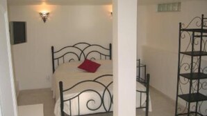 A bedroom with a bed, a nightstand, a wall-mounted lamp, and a metal shelf unit. - Villa Lysa studio in character house private pool (La Garde)