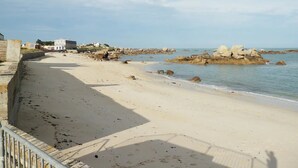 A coastal beach with a paved walkway, rocky outcrops, and a building with a white facade.