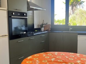 A kitchen with a stove, oven, and cabinets. There is a window with a view of greenery outside. - House / Villa - BRIGNOGAN PLAGESHouse with characterHouse with garden (Plounéour-Brignogan-Plages)