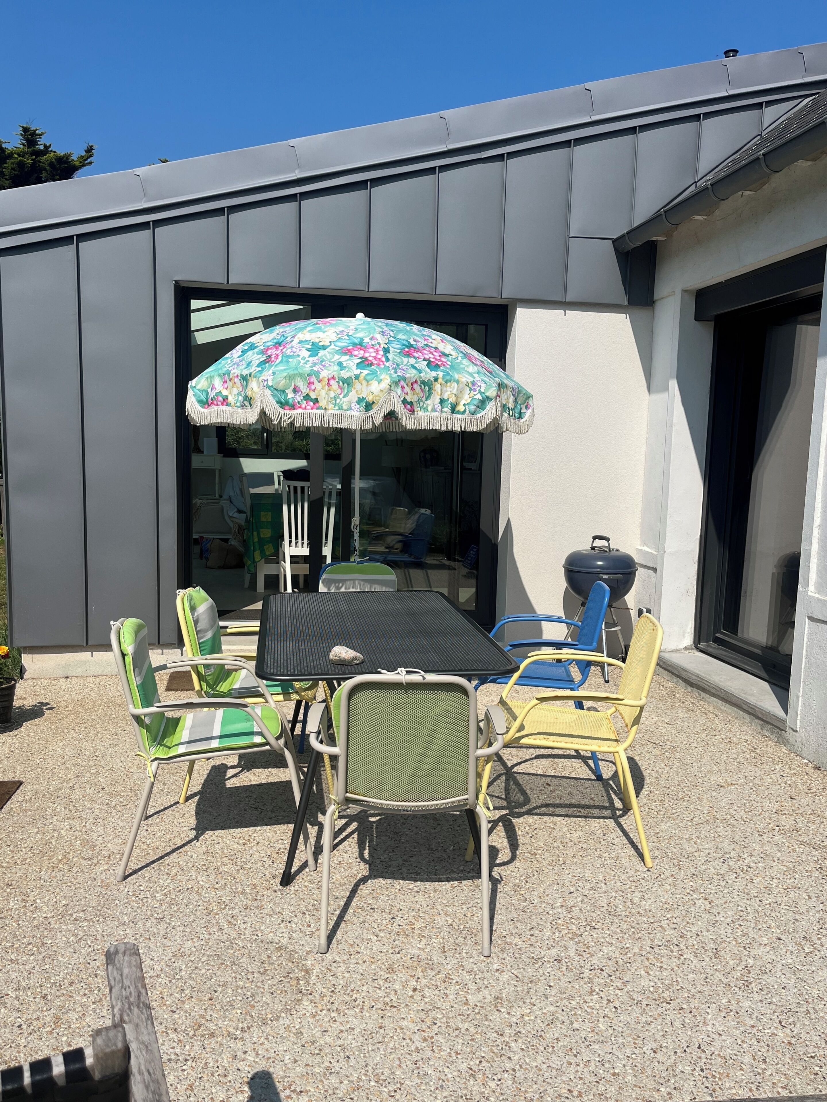 An outdoor patio with a table and chairs, a grill, and a large umbrella.