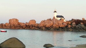 A coastal scene with a lighthouse, rocky shoreline, and a small boat.