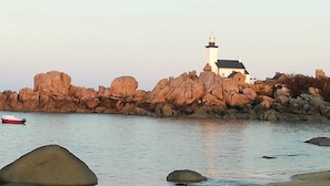 Un paysage côtier avec un phare, une côte rocheuse et un petit bateau.