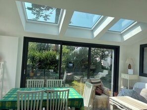 Una stanza con lucernari, un'area pranzo con tavolo e sedie, e vista su un giardino tramite ampie vetrate.