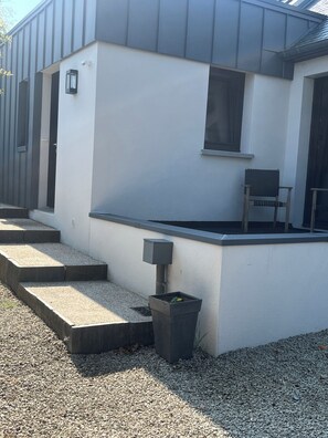 Un edificio moderno con tetto piatto, una piccola area salotto all'aperto e un cestino.
