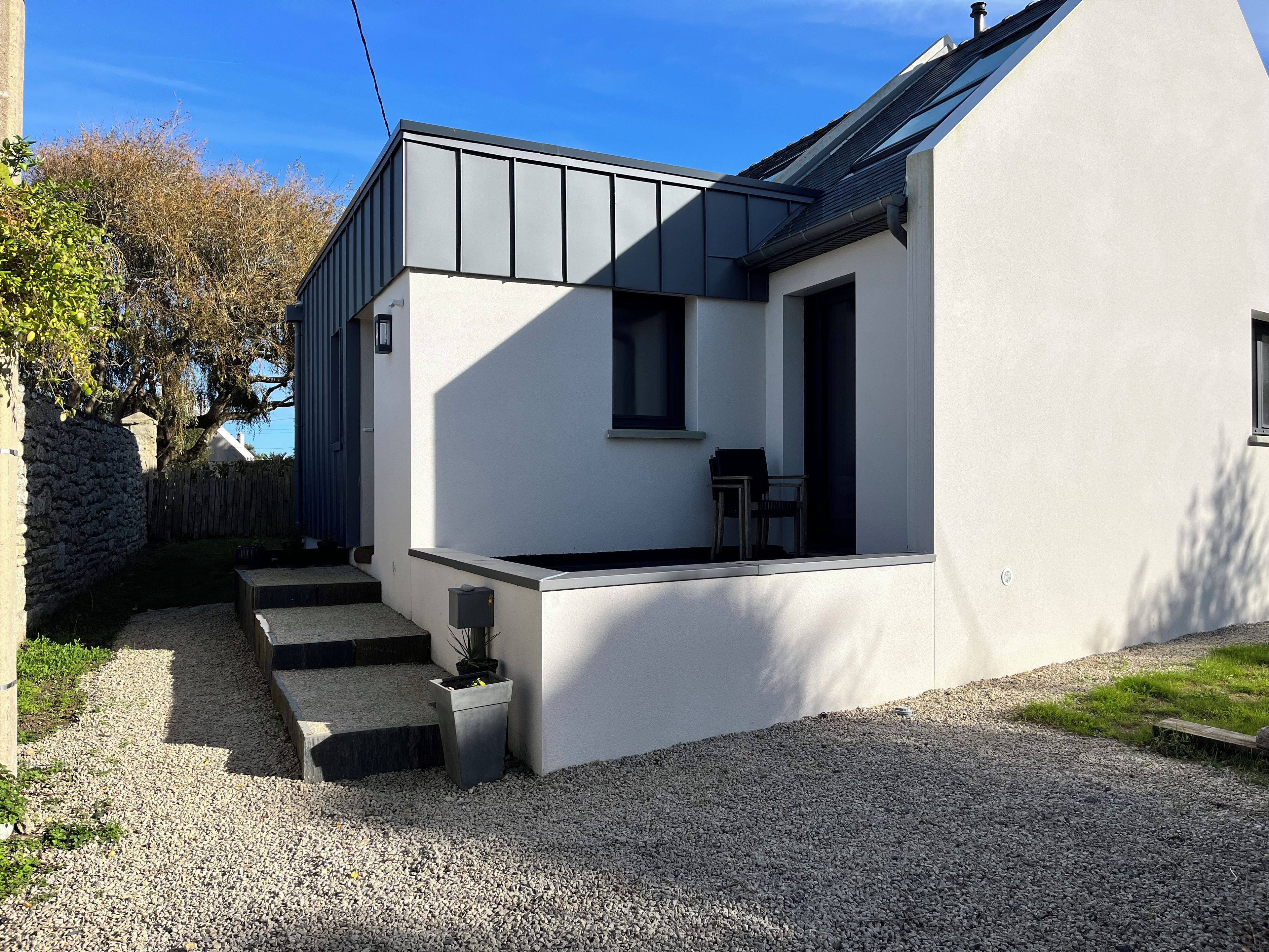 A modern house with a sloped roof, a small porch, and a gravel driveway.
