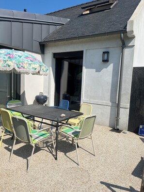 Une terrasse extérieure avec une table et des chaises, un barbecue et un parasol décoratif.