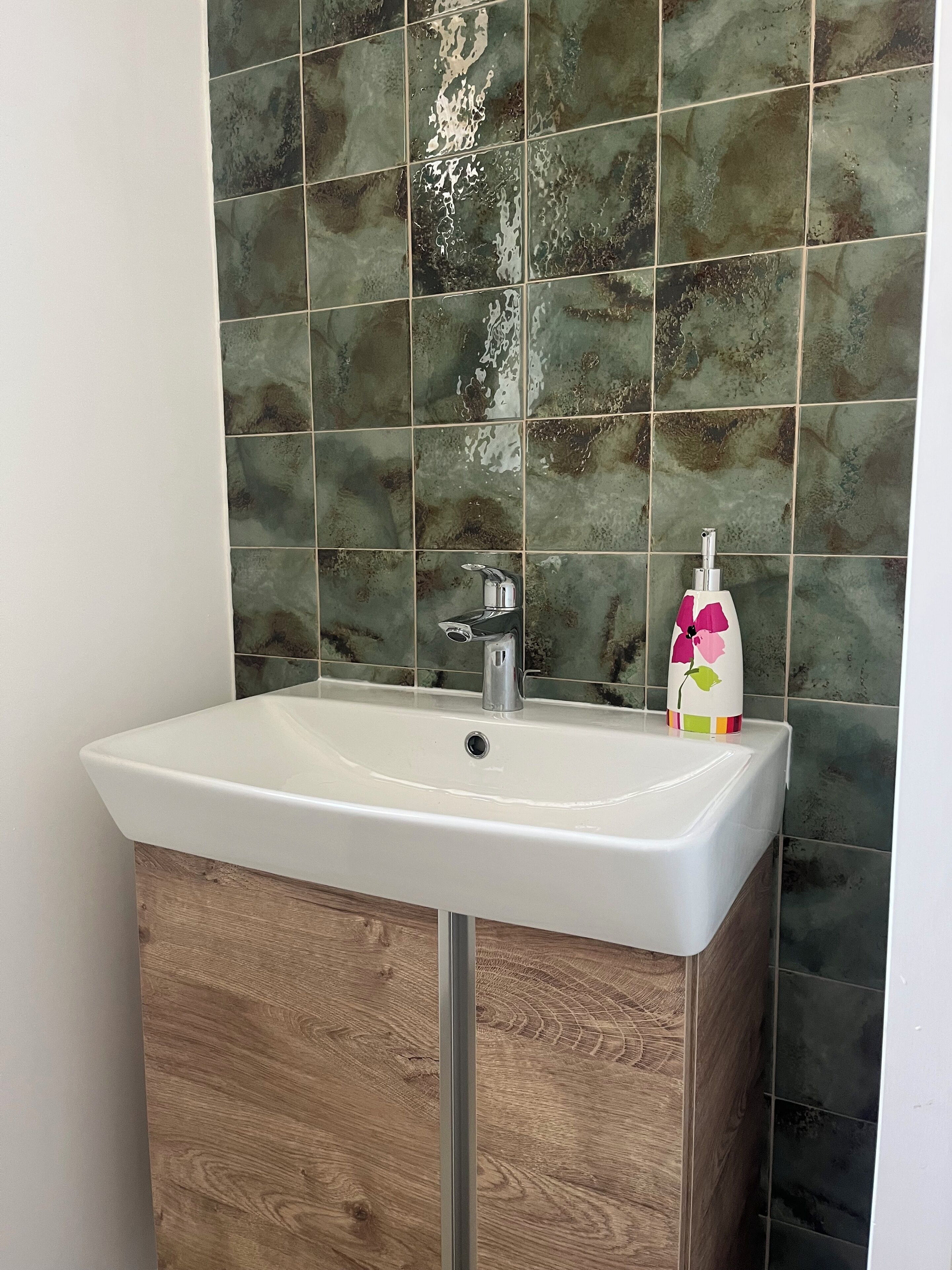 Ein Badezimmer mit einem weißen Waschbecken, einem Holzkorpus und grünen Marmorfliesen.
